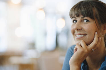 Smiling female entrepreneur looking away with hand on chin sitting in cafe - GUSF04637