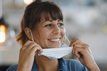 Close-up of female entrepreneur wearing protective face mask looking away while standing in cafe - GUSF04648