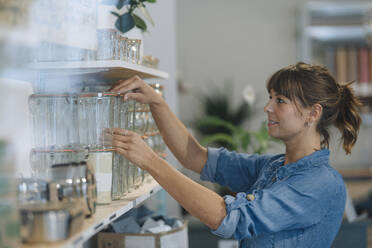 Young female entrepreneur arranging glass jar on shelf in cafe - GUSF04665