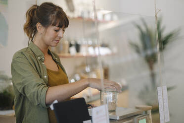 Geschäftsfrau wiegt Getreide auf einer Waage in einem Café - GUSF04669