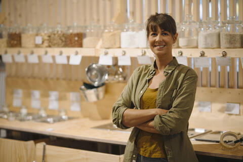 Smiling businesswoman with arms crossed standing against glass jar in cafe stock photo