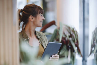 Weibliche Unternehmerin schaut weg, während sie ein digitales Tablet in einem Café hält - GUSF04680