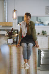 Young female owner sitting at counter in coffee shop - GUSF04685