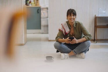 Smiling businesswoman using smart phone while sitting on floor in cafe - GUSF04689