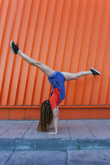 Young woman doing handstand against orange wall - MGRF00013