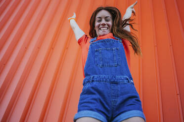 Junge Frau springt gegen orangefarbene Wand - MGRF00026