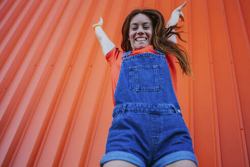 Junge Frau springt gegen orangefarbene Wand - MGRF00026