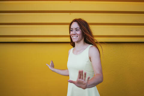 Smiling woman gesturing while standing against yellow wall stock photo