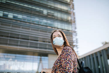 Woman in protective face mask against building in city during COVID-19 - GRCF00432