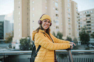 Lächelnde Frau hört Musik über Kopfhörer, während sie einen elektrischen Roller fährt - GRCF00453