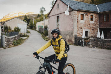 Mid adult woman in warm clothing riding mountain bike on road while traveling to Somiedo Natural Park, Spain - DMGF00238