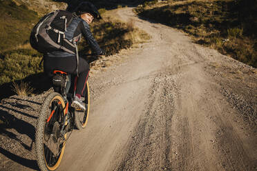 Mountainbikerin mit Rucksack auf dem Fahrrad auf einer Bergstraße im Naturpark Somiedo, Spanien - DMGF00240