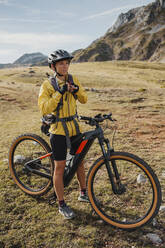 Woman in warm clothing standing on mountain bike at Somiedo Natural Park, Spain - DMGF00252