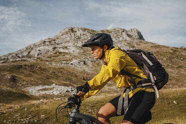 Mid adult woman with backpack riding electric bicycle on mountain at Somiedo Natural Park, Spain - DMGF00258