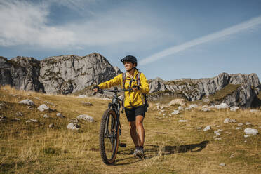 Mid adult woman holding bicycle while against mountain at Somiedo Natural Park, Spain - DMGF00260