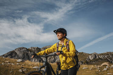 Lächelnde Frau, die mit einem elektrischen Mountainbike gegen einen Berg im Naturpark Somiedo, Spanien, fährt - DMGF00261