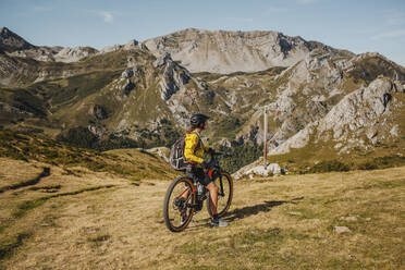 Mid adult woman on electric bicycle admiring view while standing at Somiedo Natural park, Spain - DMGF00263