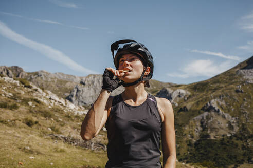 Frau mit Fahrradhelm isst einen Keks, während sie an einem Berg im Somiedo-Naturpark steht, Spanien - DMGF00264
