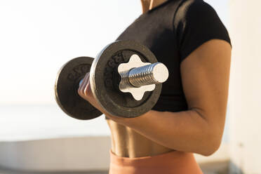 Close-up of fitness woman exercising with dumbbell during sunrise - AFVF07403