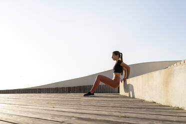 Weibliche Athletin beim Bankdrücken auf der Promenade gegen den klaren Himmel - AFVF07417