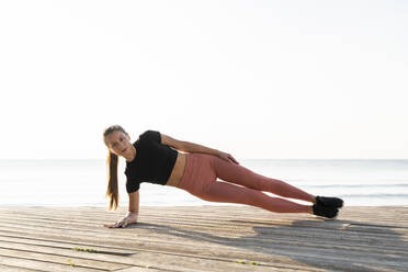 Junge Sportlerin macht Seite Planke Pose auf Promenade gegen klaren Himmel - AFVF07418