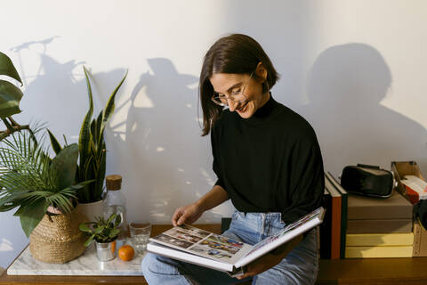 Smiling woman looking photographs in photo album while sitting at home stock photo