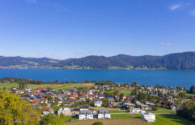 Drone view of town by lake and mountains against blue sky on sunny day, Attersee, Salzkammergut, Austria - WWF05615
