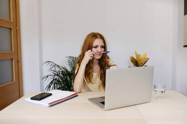 Nachdenkliche Frau, die bei der Arbeit zu Hause einen Laptop benutzt - TCEF01263