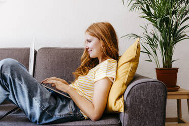 Redhead woman lying on sofa using laptop at home - TCEF01270