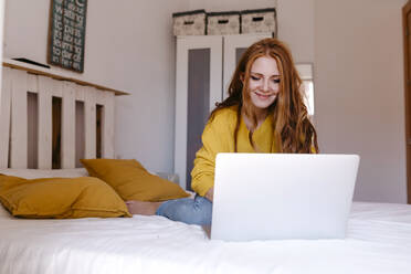 Junge Geschäftsfrau, die einen Laptop benutzt, während sie im Schlafzimmer zu Hause sitzt - TCEF01277