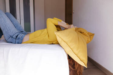 Müde Frau mit Kissen über dem Kopf liegt auf dem Bett im Schlafzimmer zu Hause - TCEF01281