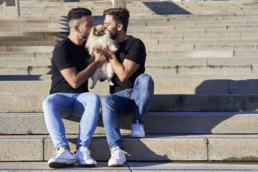 Homosexuelles Paar, das seinen Hund küsst, während es auf einer Treppe im Freien sitzt - VEGF03060
