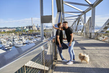 Zärtliches schwules Paar küsst sich auf einer Fußgängerbrücke an einem sonnigen Tag - VEGF03075