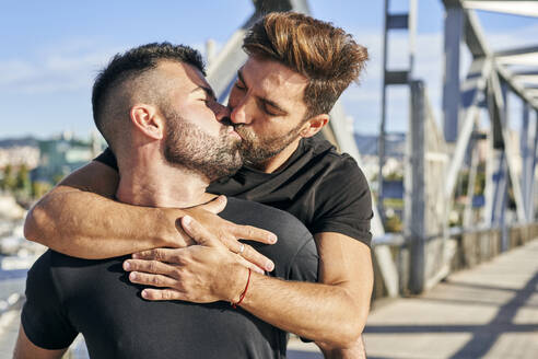 Schwuler Mann küsst seinen Freund auf einer Fußgängerbrücke an einem sonnigen Tag - VEGF03079