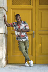 Cheerful young man standing against closed yellow doors - PNAF00034