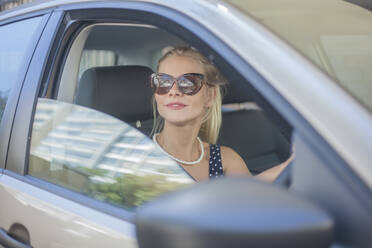 Junge Frau mit Sonnenbrille beim Autofahren in der Stadt - AJOF00489