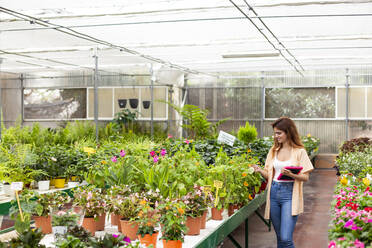 Lächelnde Geschäftsfrau mit digitalem Tablet, die eine Pflanze bei der Arbeit im Gartencenter untersucht - LJF01863