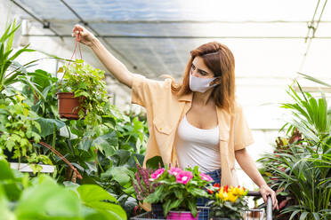 Businesswoman wearing face mask working while standing at garden center - LJF01866