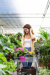 Lächelnde Geschäftsfrau, die bei der Arbeit in einem Gartencenter Pflanzen sammelt - LJF01868