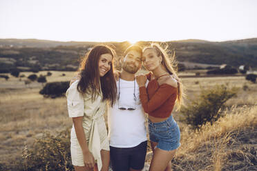 Smiling young man with female friends standing on field - RSGF00406