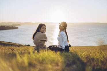 Young female friends sitting on hill at Mirador de La Providencia, Gijon, Spain - RSGF00408