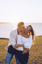 Boyfriend kissing girlfriend on hill against sky at Mirador de La Providencia, Gijon, Spain - RSGF00417