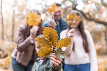 Familie versteckt Gesicht mit trockenen Blättern im Park im Herbst stehend - WPEF03516