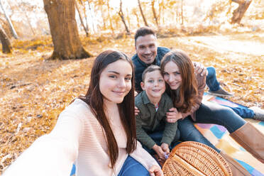Lächelnde Familie, die ein Selfie macht, während sie im Herbst im Park sitzt - WPEF03526