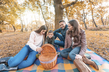 Kinder beim Öffnen eines Essenskorbs, während die Eltern im Herbst auf einer Picknickdecke im Park sitzen - WPEF03527