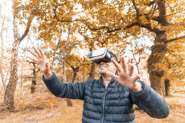 Mature man wearing virtual simulator while standing in park during autumn - WPEF03532