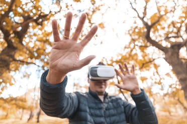 Man gesturing while wearing virtual simulator standing in park - WPEF03533