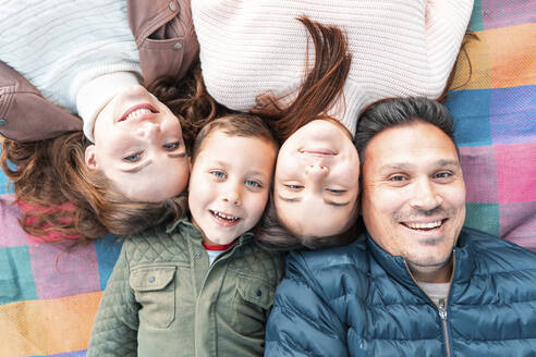 Direkt über der Ansicht einer lächelnden Familie, die auf einer Picknickdecke im Park liegt - WPEF03534
