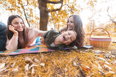 Smiling family enjoying while lying down in park during autumn - WPEF03537