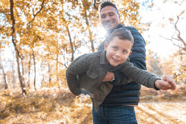 Father picking up son while standing in park during autumn - WPEF03541